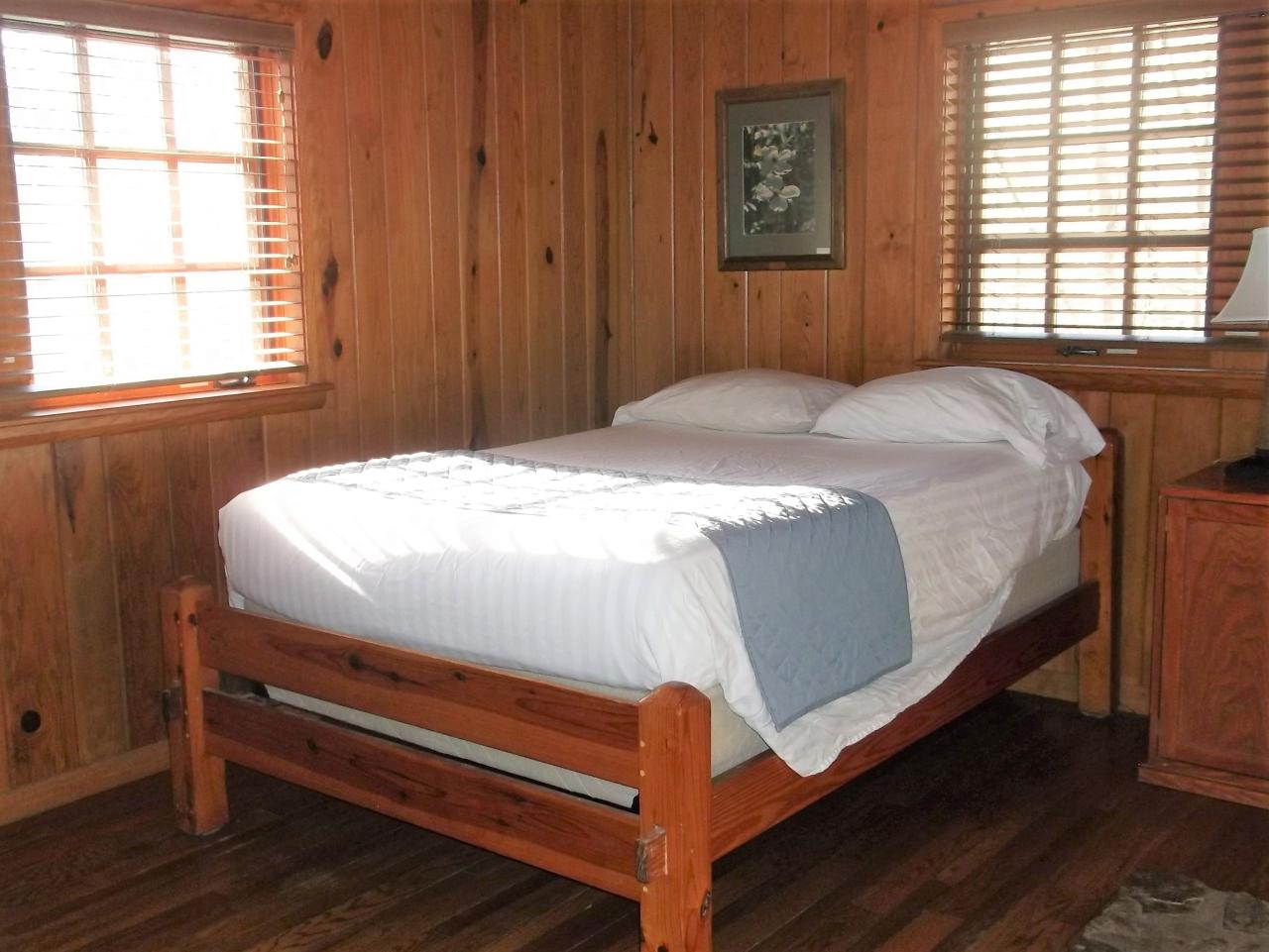 A view of the bedroom in cabin 15 including a bed, dresser and two exterior windows